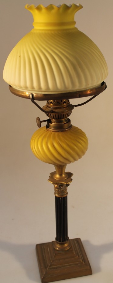 An early 20thC oil lamp with opaque yellow glass reservoir and shape on columnar base 47cm high.