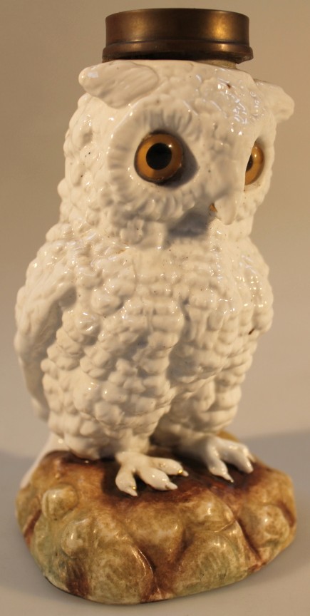 A 19thC German porcelain owl novelty lamp base, with glass eyes, perched on a rocky mound, unmarked,