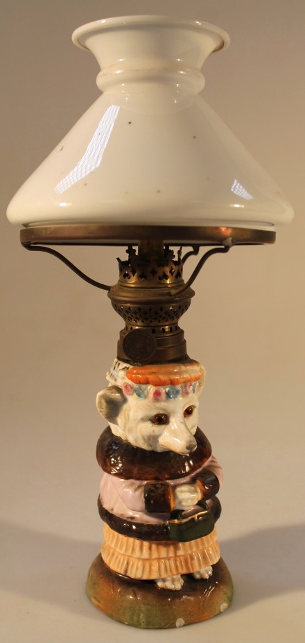 A 19thC German porcelain oil lamp, the base modelled as a bear, wearing a fur trimmed jacket and