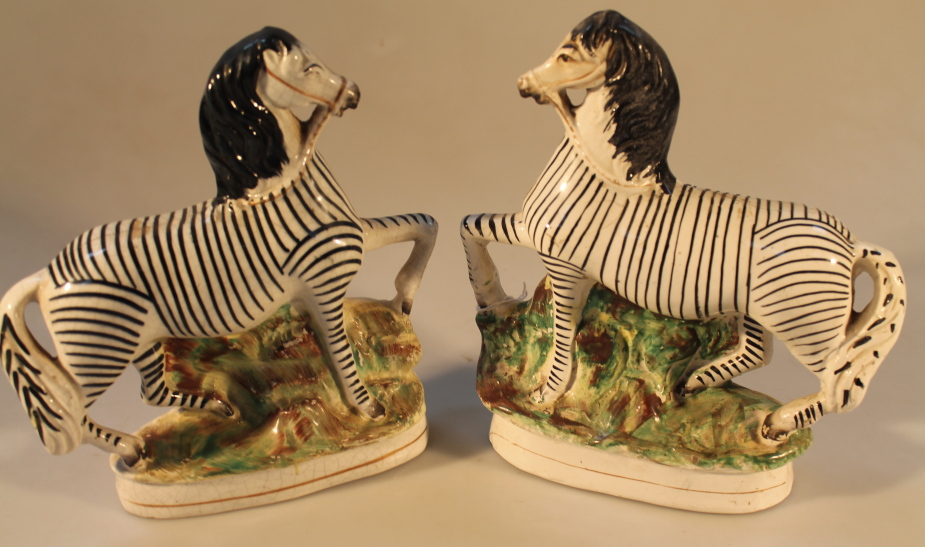 A matched pair of 19thC Staffordshire zebra, each modelled with a raised foreleg against a mossy