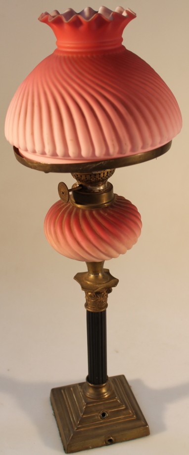 An early 20thC oil lamp, with opaque red glass reservoir and matching shade of columnar base, 45cm