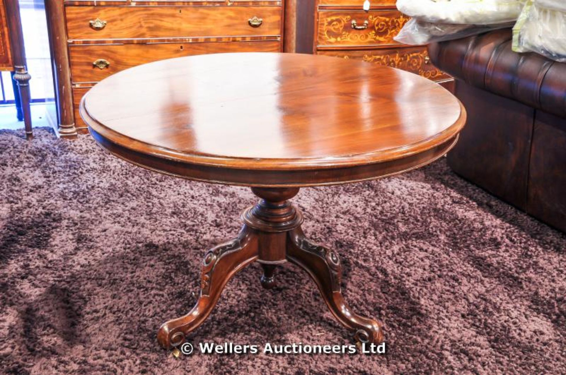 A mahogany tilt top table sitting on turned pedestal with carved tripod legs and original castors,