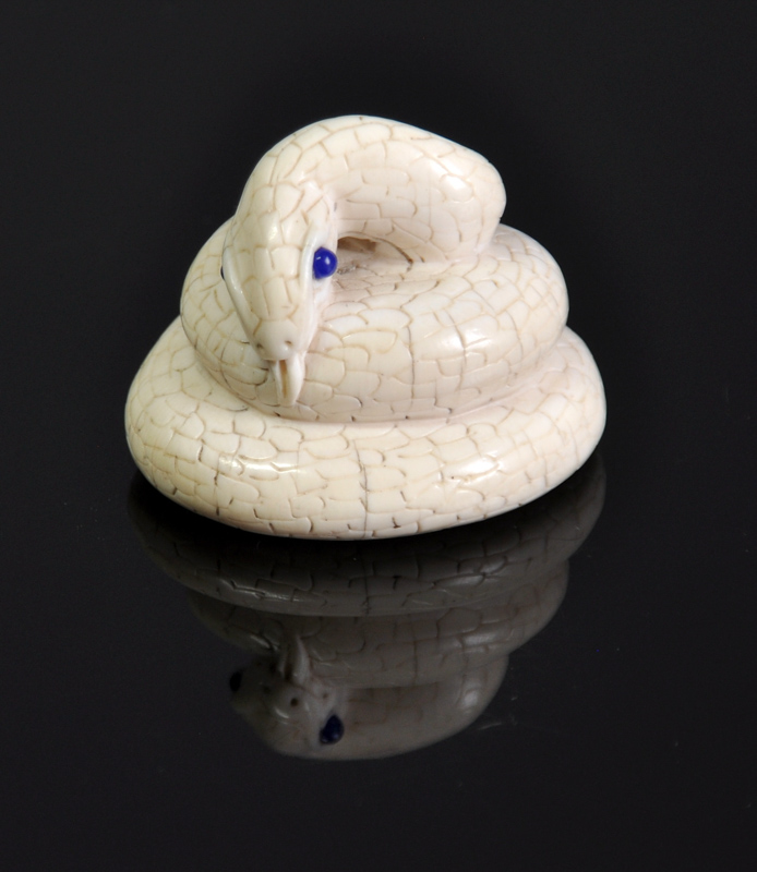 An ivory netsuke of a coiled snake, blue stone eyes, signed