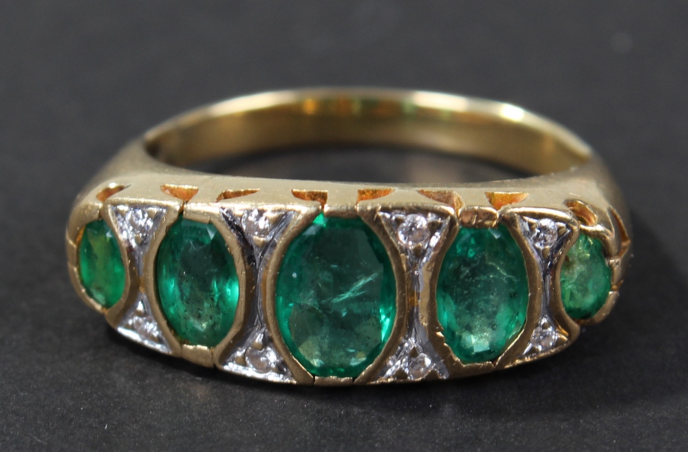 Yellow metal diamond and emerald set ring, set with a row of five oval cut emeralds and eight