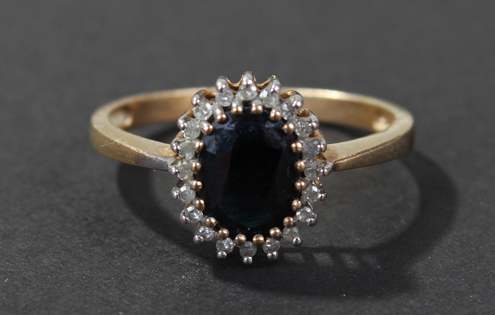 9 carat gold diamond and blue sapphire set ring, centered with oval cut blue sapphire, surrounded by