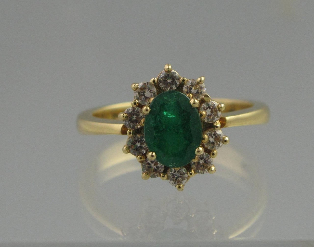 AN 18CT GOLD EMERALD AND DIAMOND CLUSTER RING, the oval mixed cut emerald 8mm x 6mm surrounded by