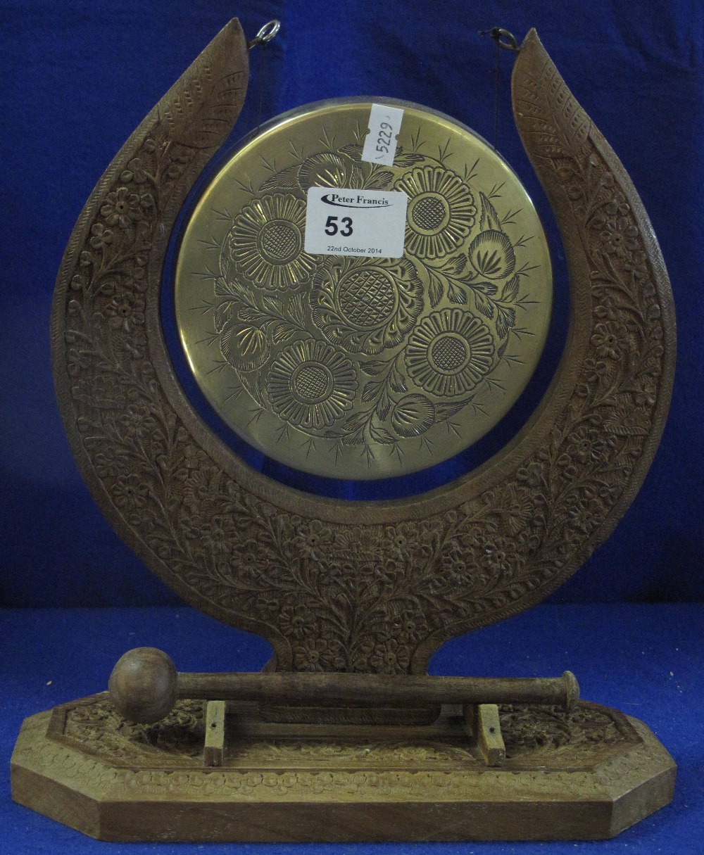 Eastern engraved brass gong on foliate carved wooden stand with striker.