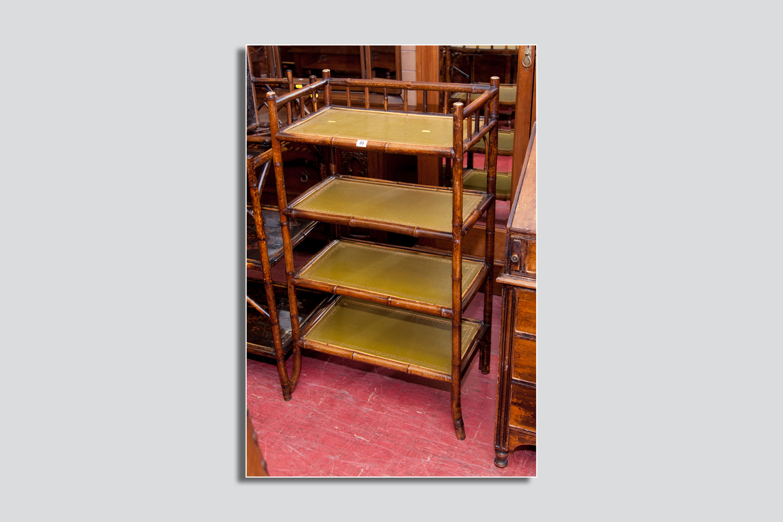 A bamboo four shelf stand, the raffia shelves surmounted with green gilt tooled leather skivers, 43