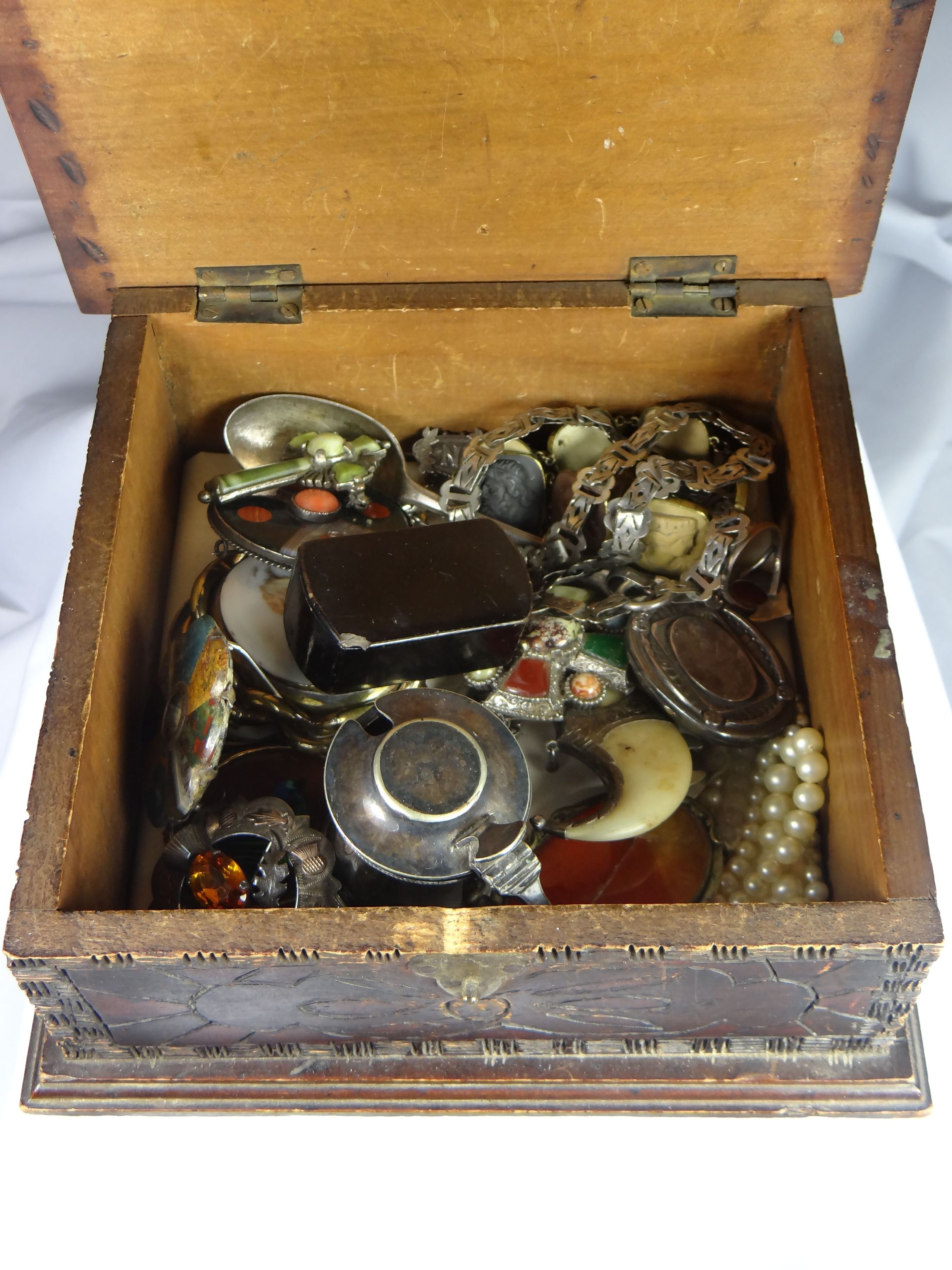 A primitive carved wooden box containing a parcel of mixed jewellery and collectables including