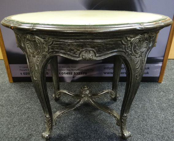 A carved ebonised shaped oval side-table with inset-glass top, having acanthus supports and four