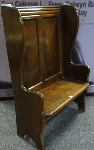 A neat polished oak winged settle with shaped arms and supports and two fielded panels to the back,