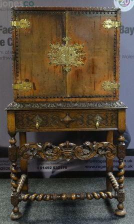 A two-door cabinet-on-stand, the base with barley-twist stretcher and supports and having a carved