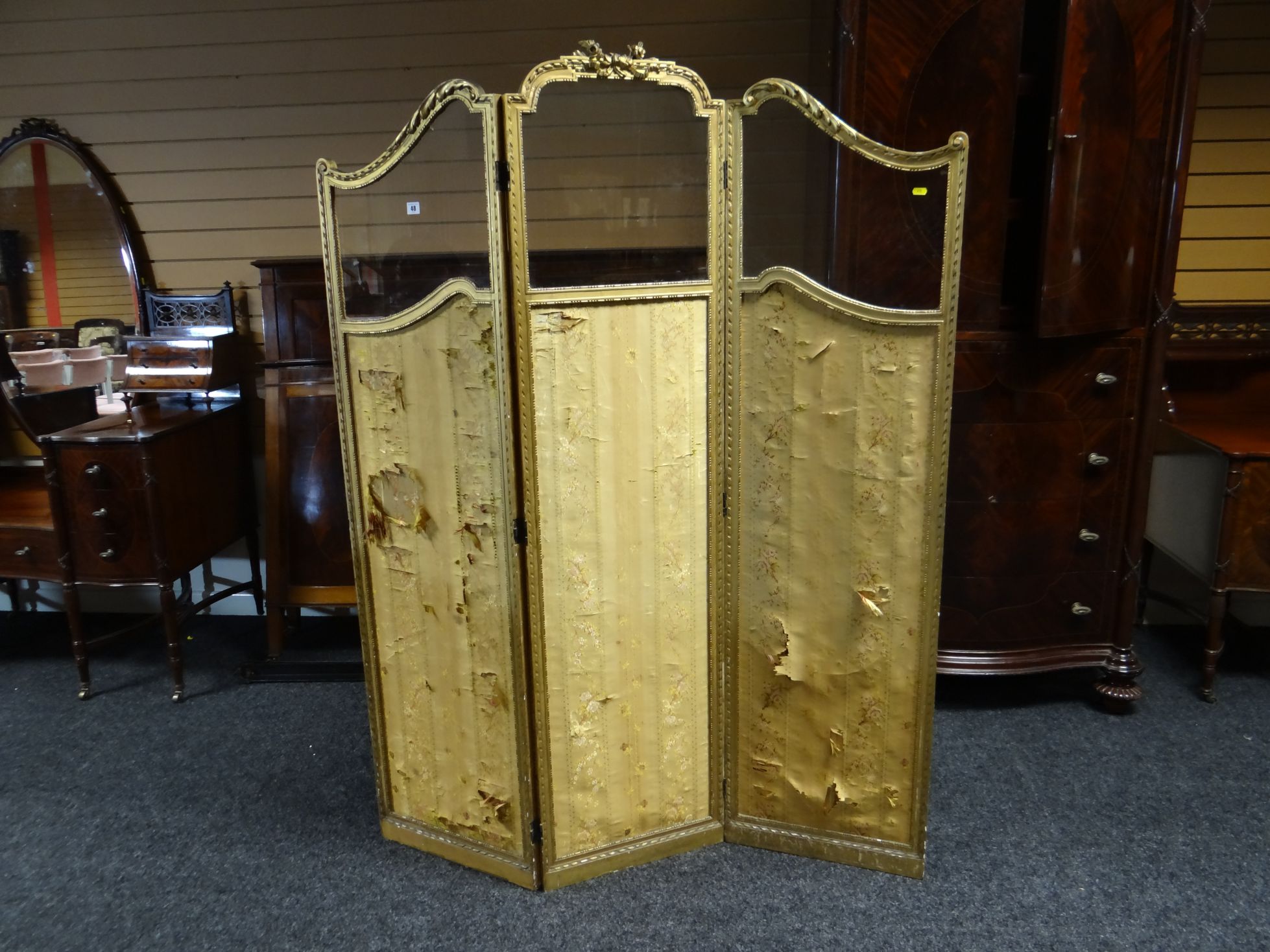 A three-fold gilt-framed semi-glazed dressing screen of shaped form and with applied ribbon and