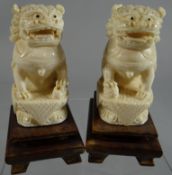 A pair of Chinese ivory carved seated lion-dogs on cushions, mounted to wooden bases, 4.5ins high (