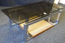 A coffee table by Pieff having a smoky-glass top on a geometric chrome base and wicker floor-level