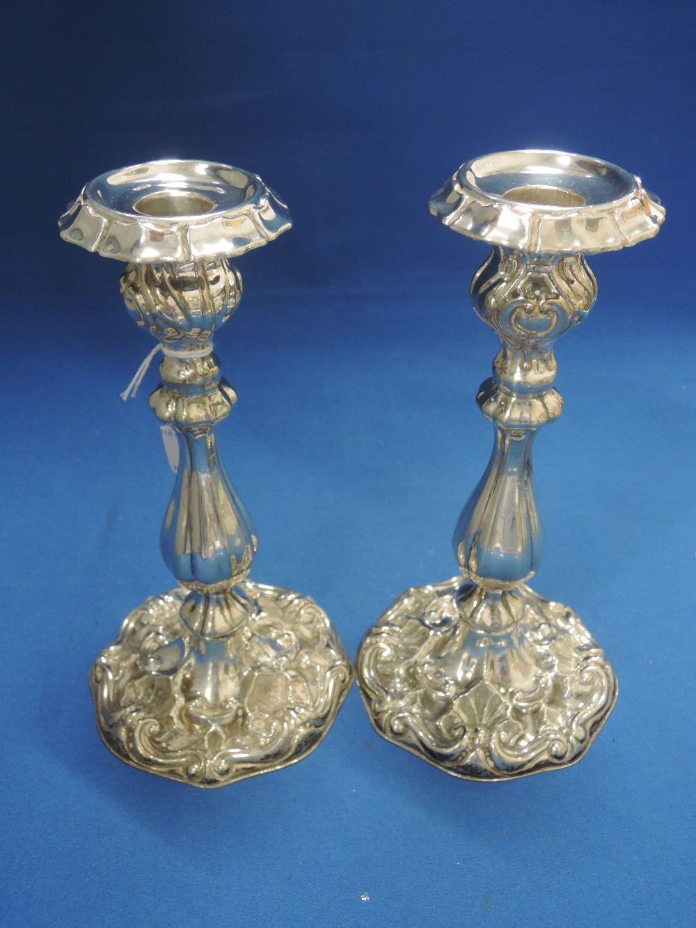 A pair of white metal candlesticks having shell and scroll decoration, circular feet and frilled