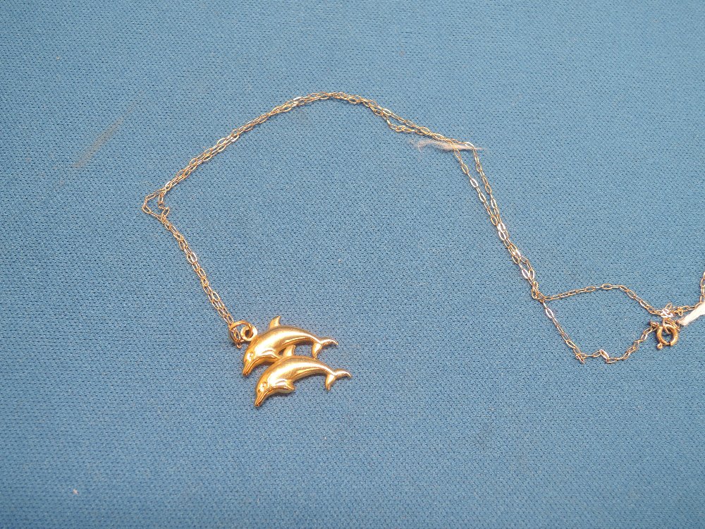 A yellow metal pendant in the form of two leaping dolphins on a yellow metal chain stamped 9k