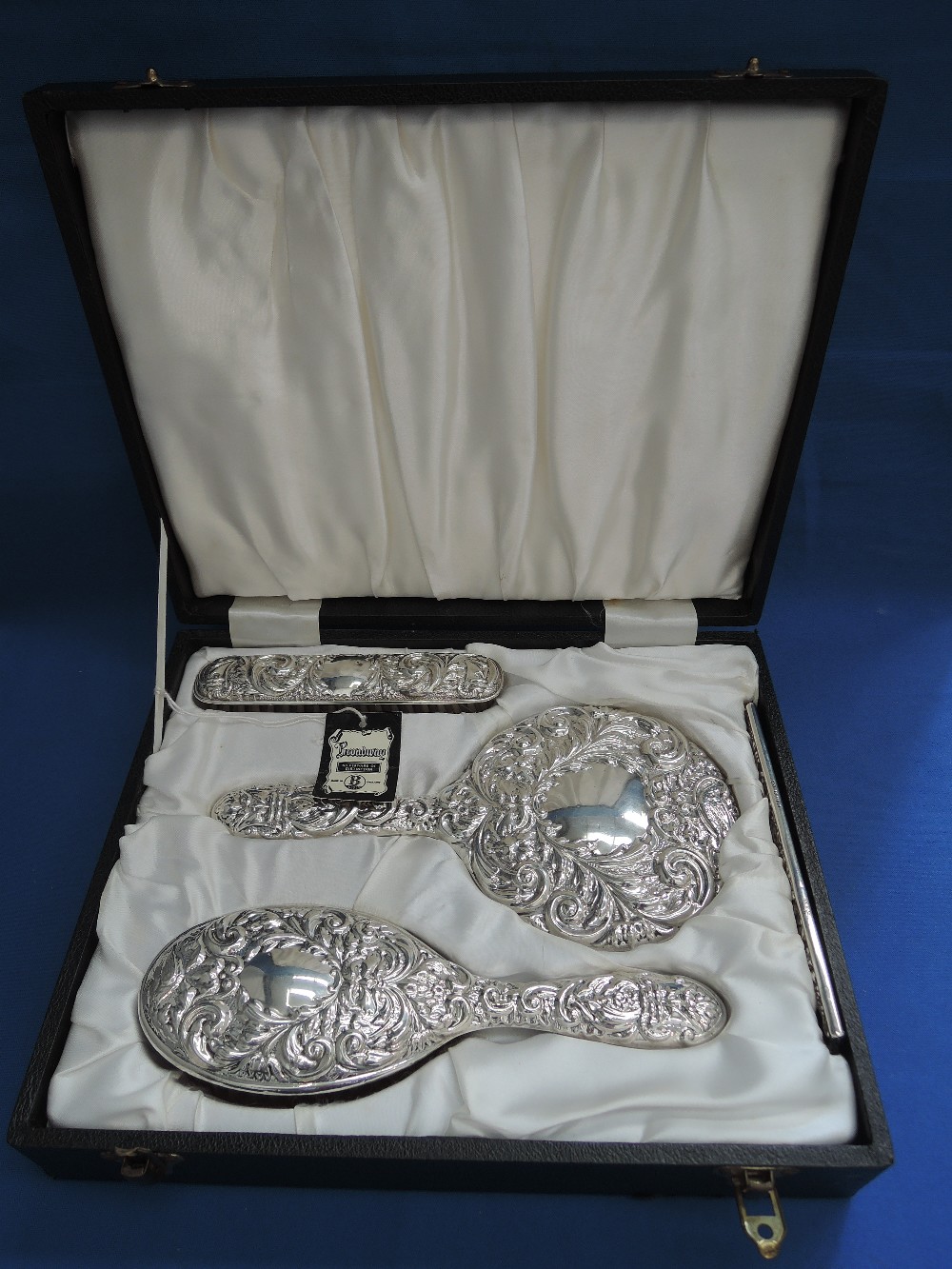 A cased four piece silver backed dressing table set having extensive scroll and foliate repousse