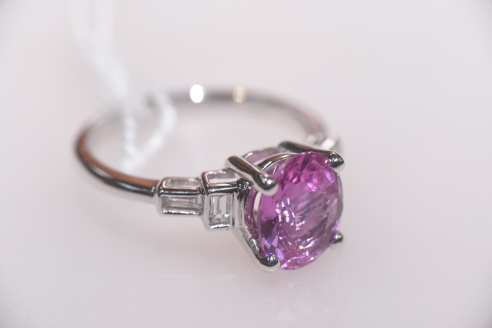 A pink sapphire and diamond ring, the oval-cut pink sapphire flanked by collet-set baguette