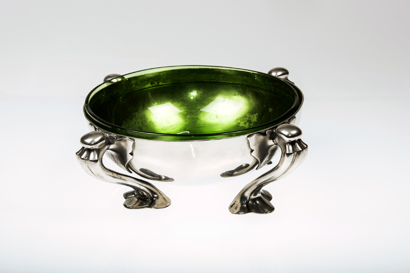 A LIBERTY & CO. PEWTER BOWL, DESIGNED BY OLIVER BAKER, with green glass liner, raised on four