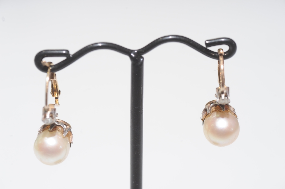 A pair of cultured pearl and diamond earrings, each pearl beneath a claw-set diamond on yellow metal