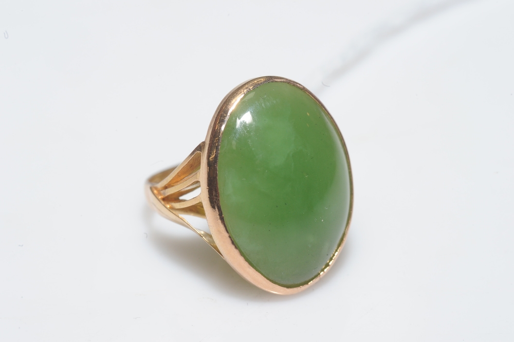 A large jade cabochon ring, the oval stone approx. 22mm by 16mm collet-set in yellow gold, on a