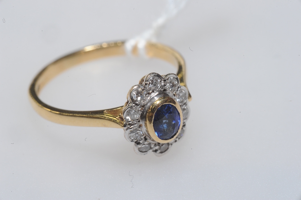 A sapphire and diamond cluster ring, the oval-cut sapphire collet set within a band of brilliant-cut