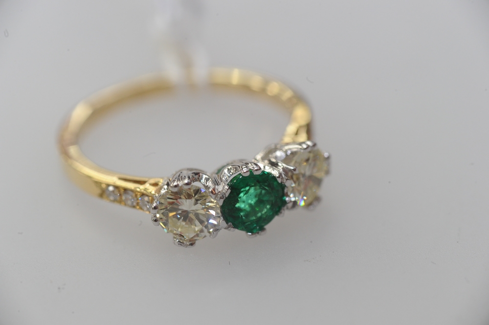 An emerald and diamond three-stone ring, the round-cut emerald flanked by a pair of round