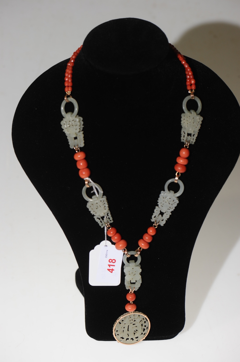 A coral and jadeite necklace, the circular pierced pendant suspended from five pierced plaques