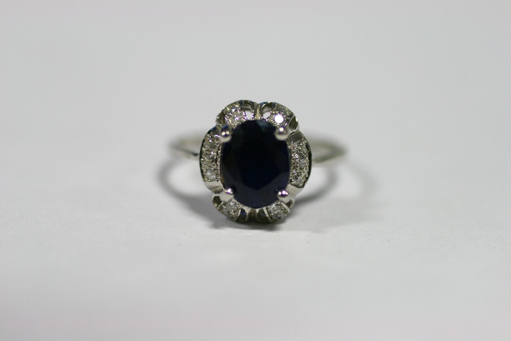 A sapphire ring, the oval-cut blue stone set within a border of small white sapphires to a 925