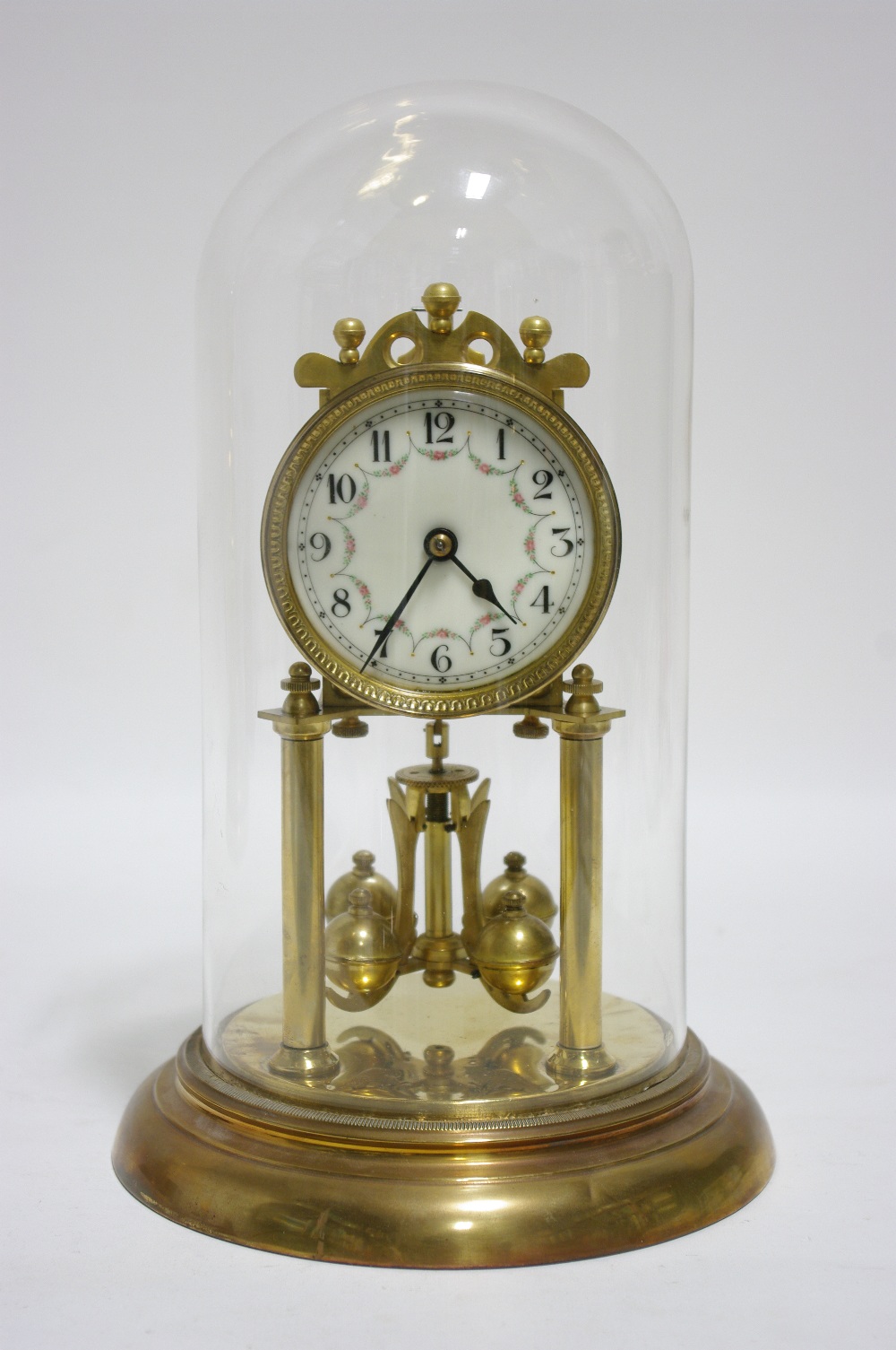 A similar brass timepiece with floral decorated 3"" diam. dial, 10"" high; under glass domed dust