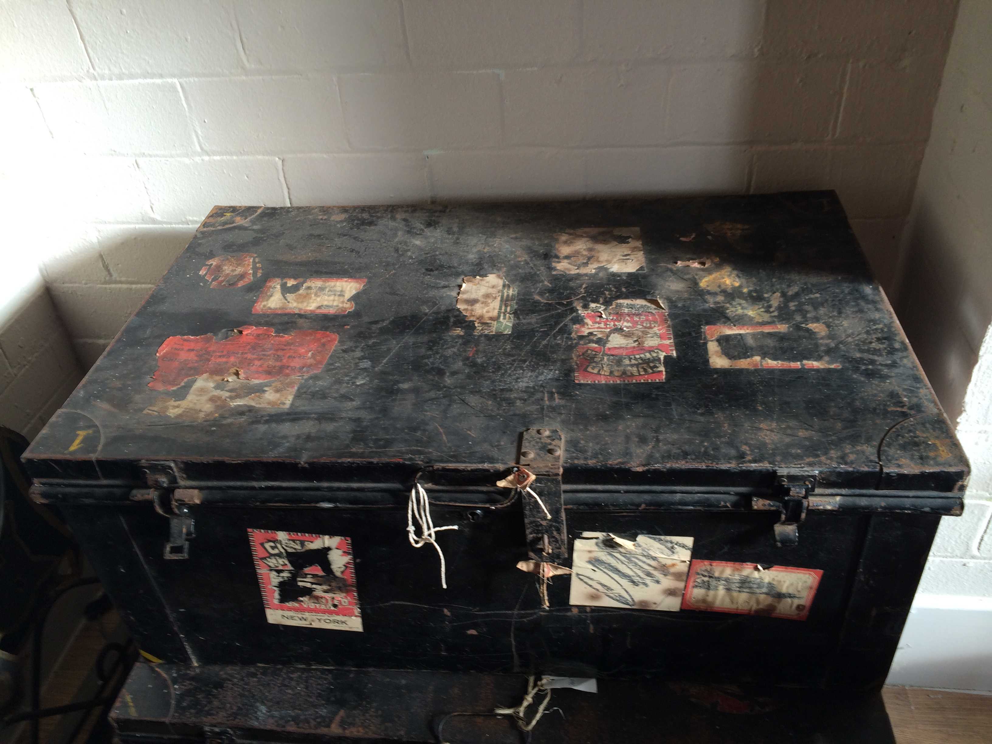 Large, decorative metal trunk, painted black with original usage stickers. Heavy hinged lid with