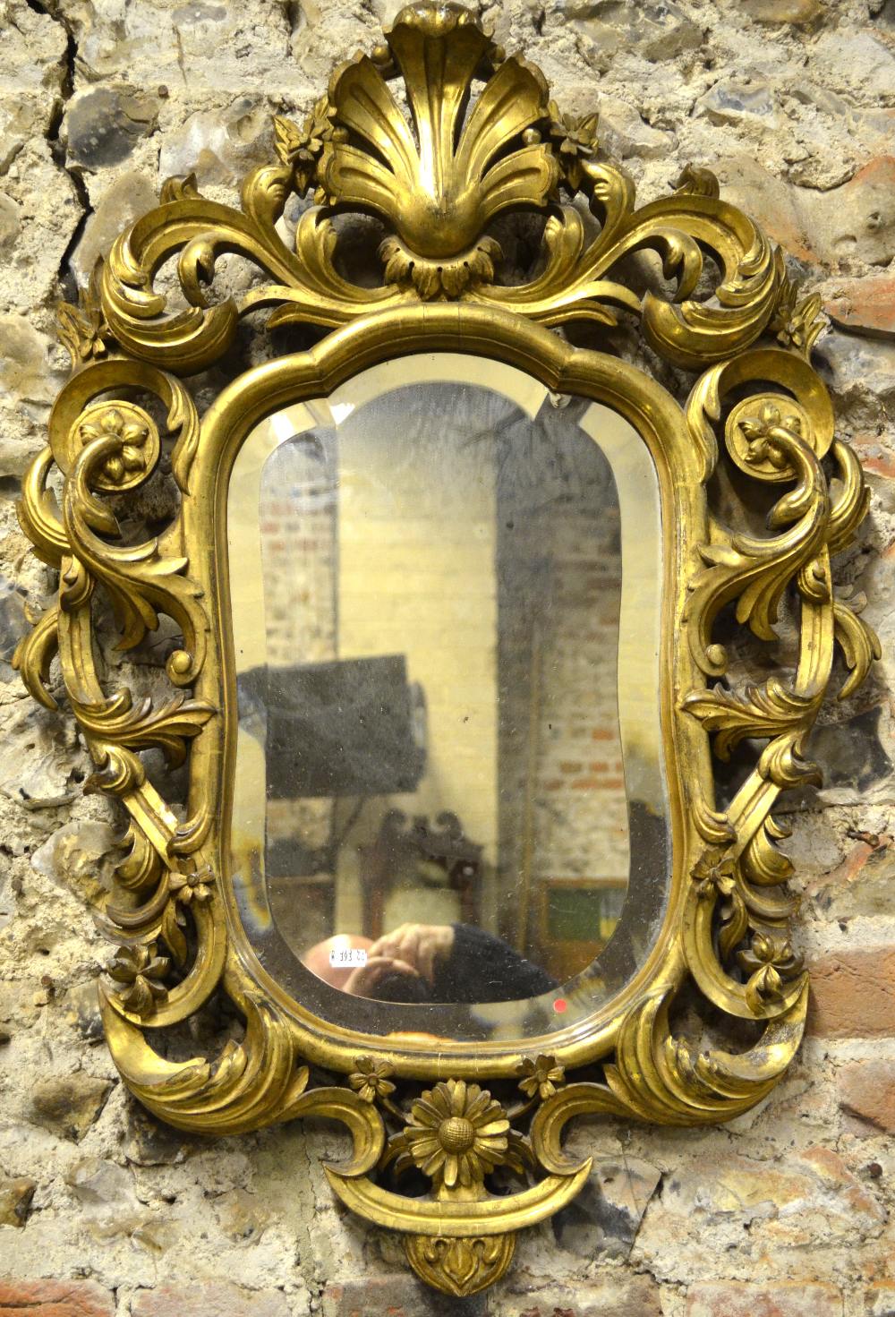 A 19th century carved giltwood mirror with shaped bevelled plate, surmounted by an open shell form