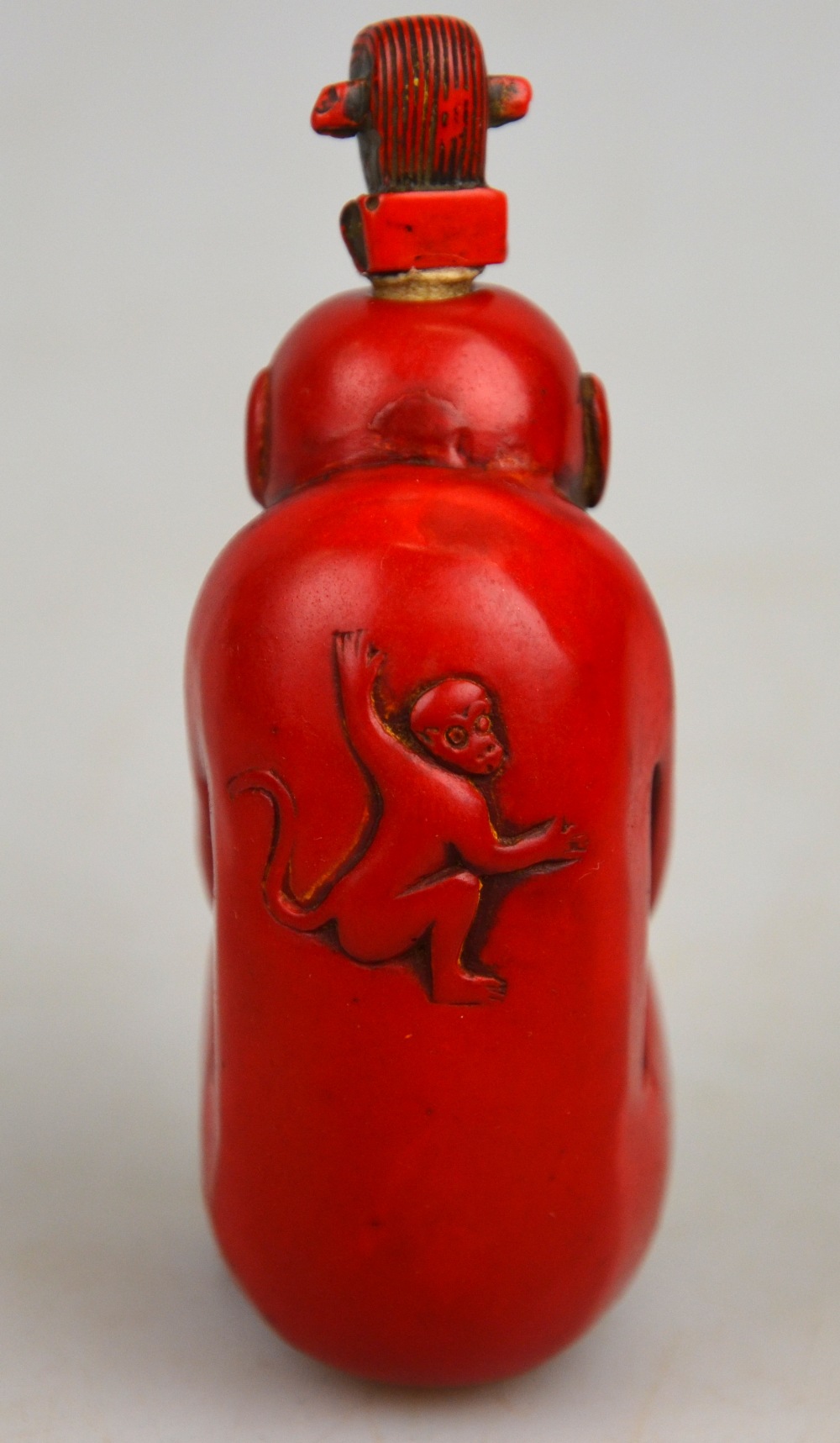 A Chinese red coloured hardstone snuff bottle and stopper in the form of a monkey, 8.5 cm - Image 2 of 3