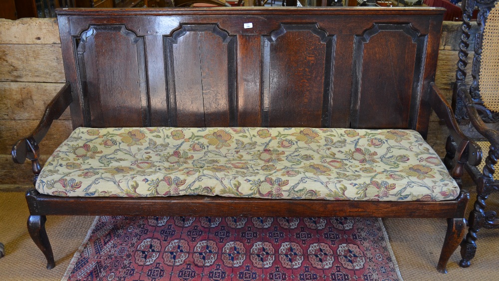 An 18th century oak settle, the four panel back over shaped arms and raised on club front legs, 183