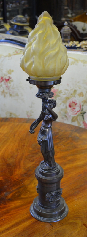 A bronze newel-post lamp with frosted amber glass flambeau shade supported by the figure of a