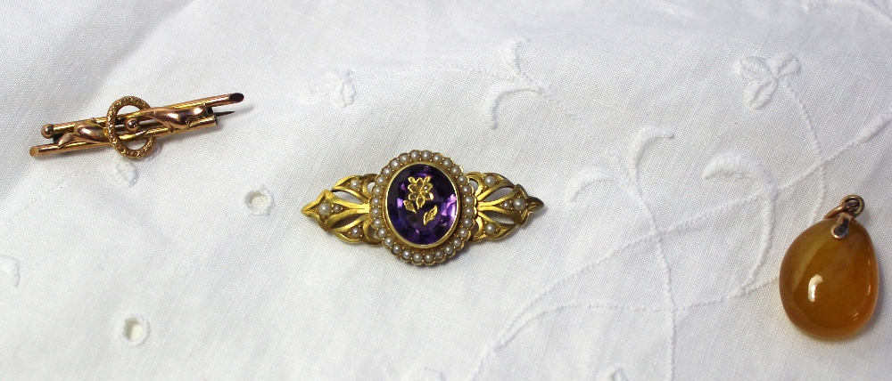A yellow metal bar brooch with a central oval amethyst inset with a floral design surrounded by seed
