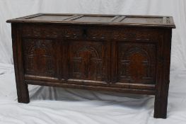 An 18th century style oak coffer, the panelled top above a carved frieze and three panels on stiles,