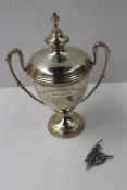 An Elizabeth II silver lidded trophy cup with a turned finial and leaf capped handles on a spreading