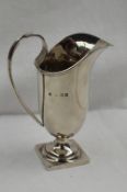 An Edward VII silver helmet shaped cream jug with a scrolling handle on a spreading base and
