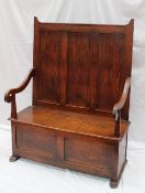 A 19th century oak box settle, the panelled back with scrolling arms above a hinged seat, panelled