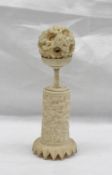 A Chinese ivory puzzle ball carved with flowerheads and leaves on a column carved with figures,