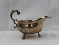 A George V silver sauce boat, with a flared rim and leaf capped scrolling handle on three legs and