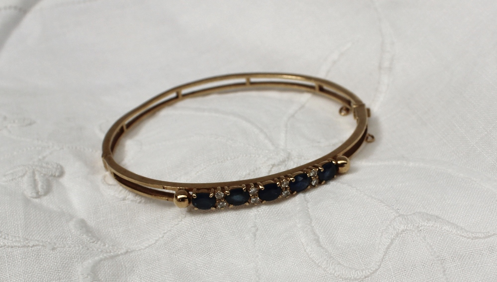 A 9ct yellow gold hinged bangle set with five oval sapphires interspersed with eight brilliant cut