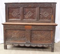 An 18th century oak coffer, the planked top now fixed, above a carved frieze and three panels on the