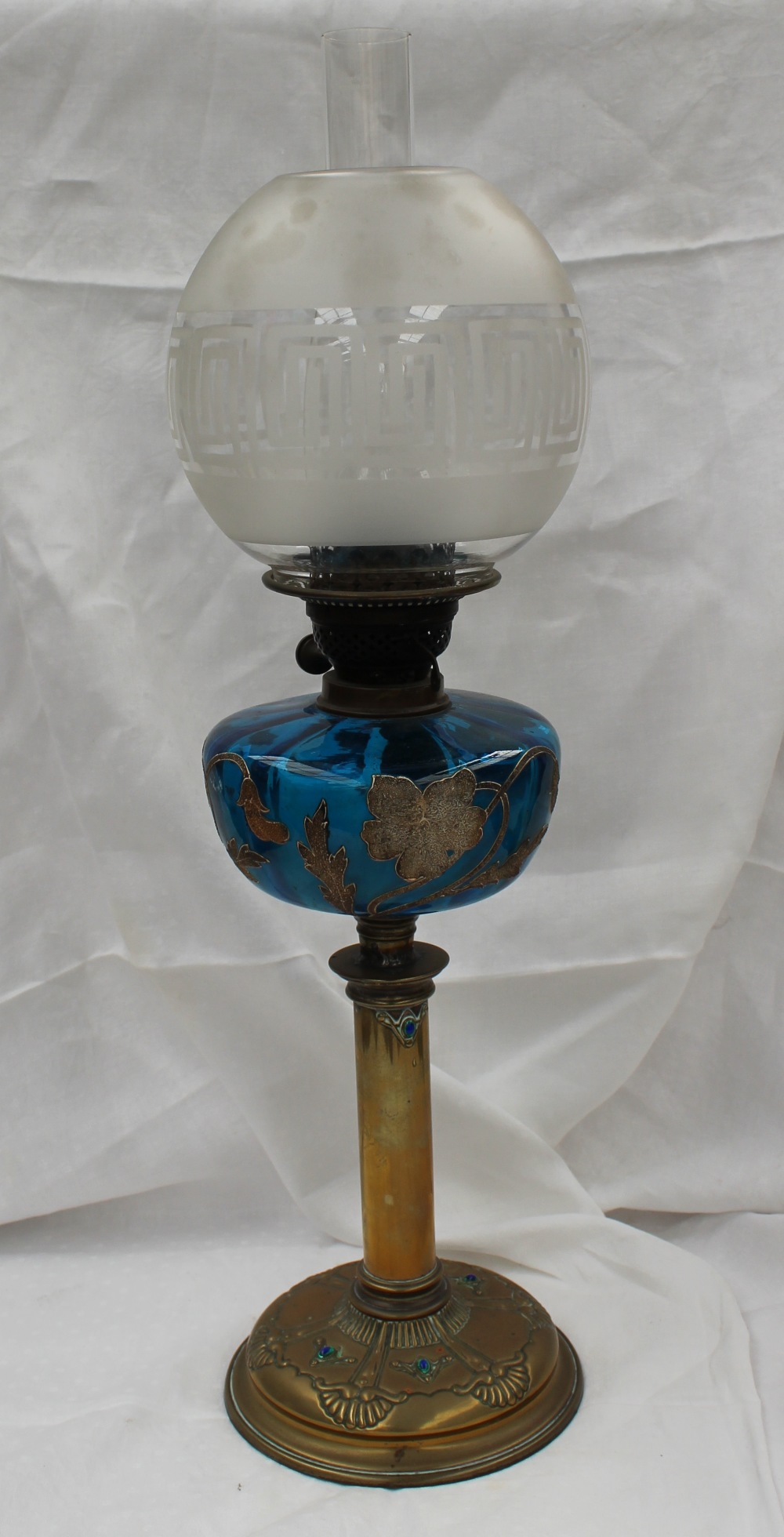 A Victorian oil lamp with an etched glass globe shade above a blue glass reservoir decorated with