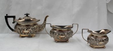 An Edward VII silver three piece teaset embossed with flower heads and leaves on flattened bun feet,
