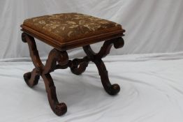 A Victorian walnut framed stool with a pad upholstered top on an X frame with a turned central pole