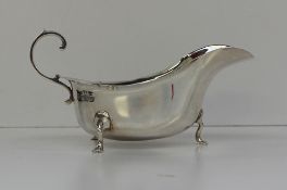 A George V silver sauce boat with a flared rim and C scroll handle, on three cabriole legs and pad