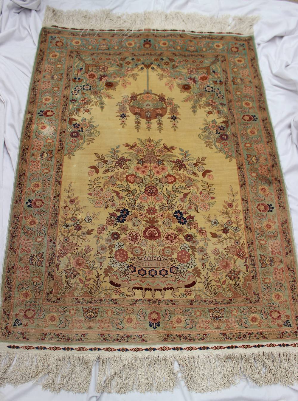 A Turkish silk rug, with a cream ground decorated with a vase of flowers and a hanging basket of